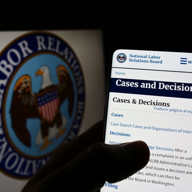 A hand holding a phone with the NLRB logo in the background