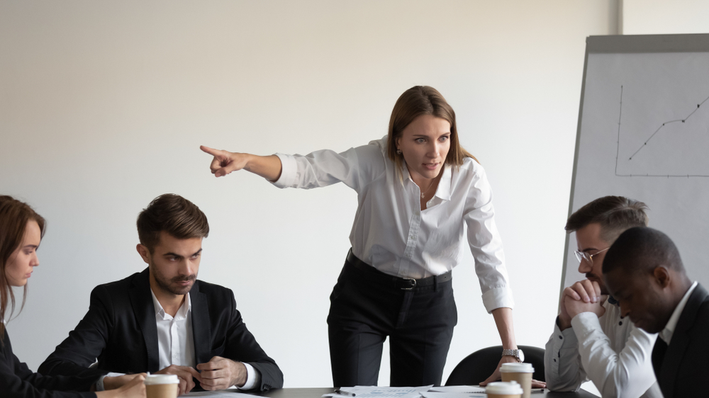 Standing woman berating people seated at a table.