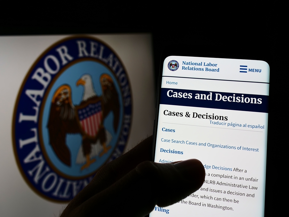 A hand holding a phone with the NLRB logo in the background